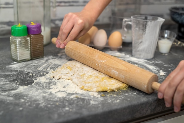 En una mesa grande y espaciosa, una mujer prepara la cena donde rompe los huevos y amasa la masa para la cazuela Concepto de cocina