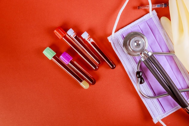 Mesa de laboratorio con tubo de ensayo médico con sangre para el virus de la neumonía atípica máscara de fonendoscopio