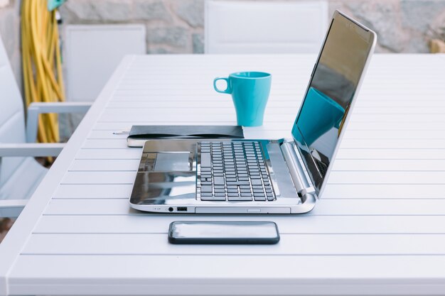 Mesa con laptop, teléfono, notebook y taza, para teletrabajo en el jardín de su casa