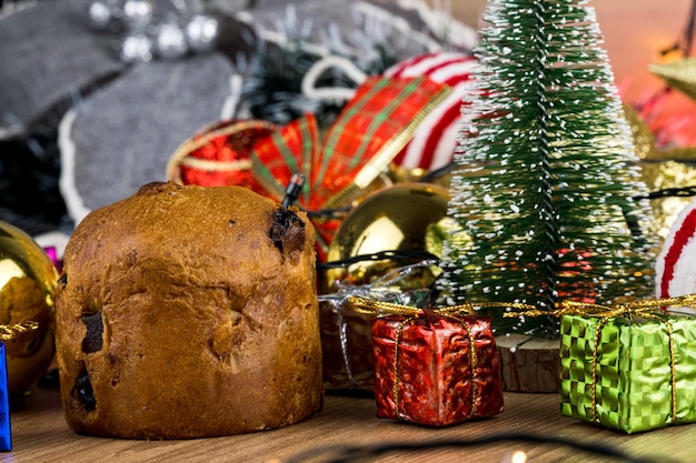 Mesa de madera con adornos navideños. Bolas rojas, plateadas y doradas, cajas de regalo, luces, panettone, árbol de Navidad y otros. Enfoque selectivo.