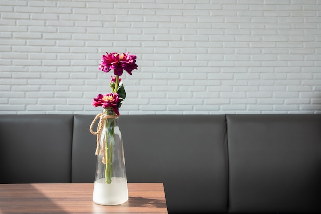 Mesa de madera con flor de zinnia en jarrón de vidrio.