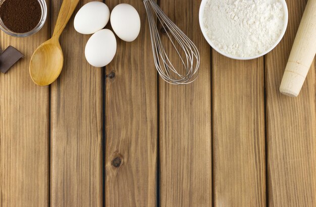 Una mesa de madera con harina, huevos y un batidor.