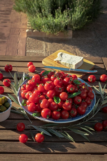 Mesa de madera en el jardín con tomates cherry, aceitunas y plato con queso gorgonzola. Saludable