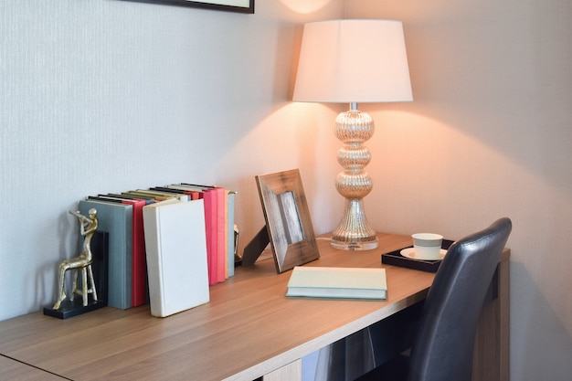 Mesa de madera con lámpara de lectura y libros en interior moderno de sala de trabajo