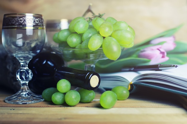 Mesa de madera con libro de botellas de vino y uva.