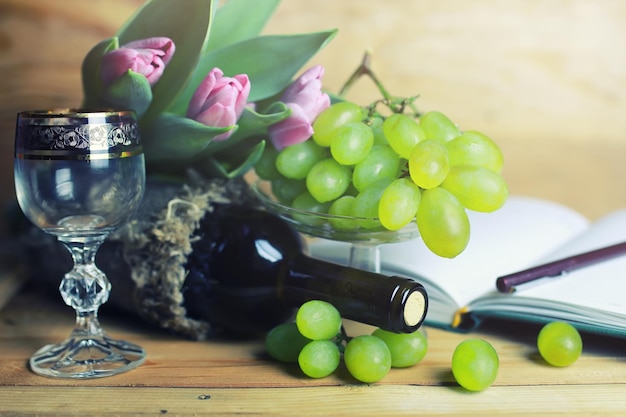 Mesa de madera con libro de botellas de vino y uva.