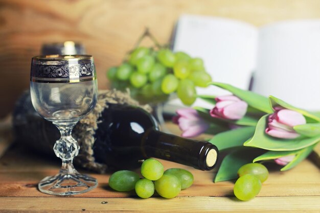 Mesa de madera con libro de botellas de vino y uva.