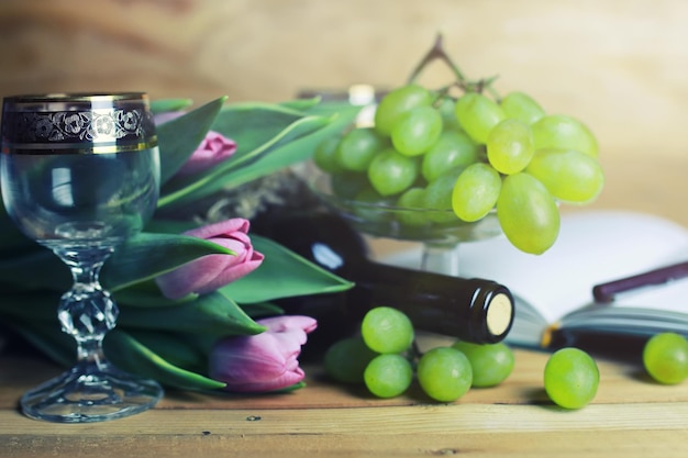 Mesa de madera con libro de botellas de vino y uva.