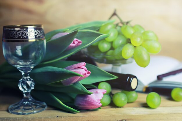 Mesa de madera con libro de botellas de vino y uva.
