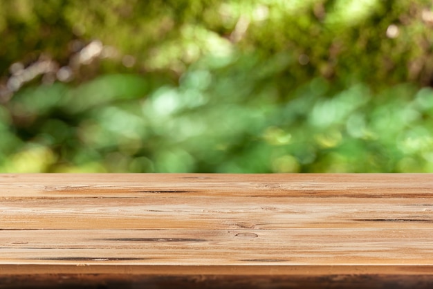 Mesa de madera natural en blanco sobre un fondo de hojas verdes borrosas con bokeh para demostración y montaje de sus productos y cosas.