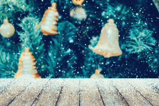 Mesa de madera con nieve y campanas doradas decoradas en árbol de Navidad