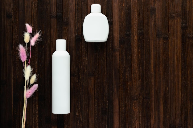 En una mesa de madera oscura hay botellas blancas vacías con cosméticos y flores secas El concepto de tratamiento cosmético para el cuidado de la piel y el cuerpo preservación de la juventud