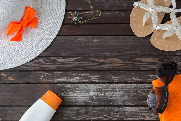 En una mesa de madera, sandalias, lentes de sol, toalla, sombrero, crema solar.