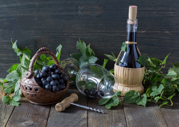 En una mesa de madera, uvas oscuras en una cesta, vino tinto, una copa de vino y un sacacorchos.