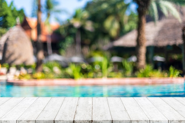 Mesa de madera vacía y piscina borrosa en resort tropical en verano