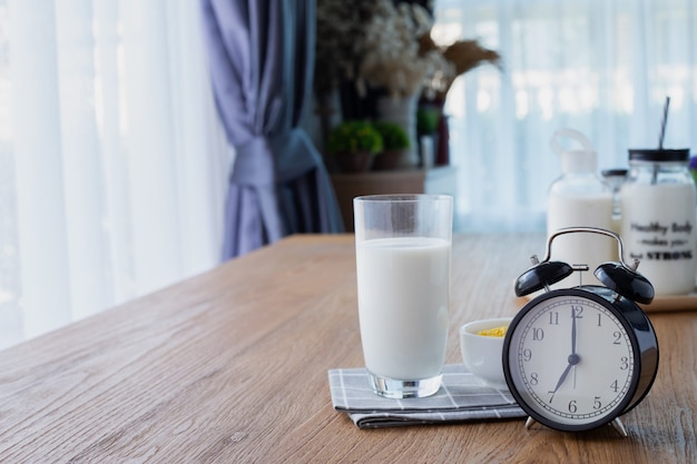 Mesa de madera con vaso de leche y despertador retro en la sala.