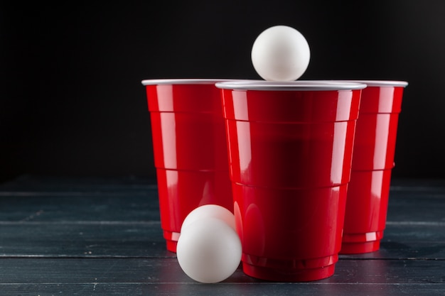 Mesa de madera con vasos rojos y bola para cerveza pong