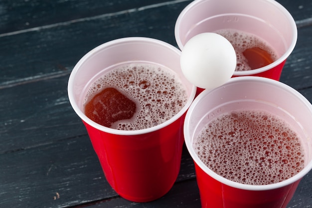 Mesa de madera con vasos rojos y bola para cerveza pong