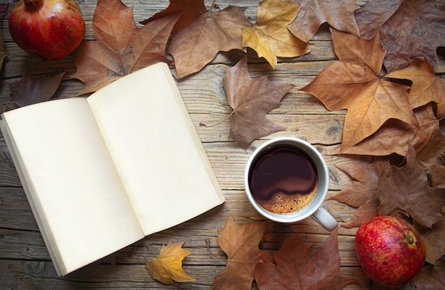 Mesa de madera vieja con libro abierto y páginas en blanco hojas secas de otoño y taza de café