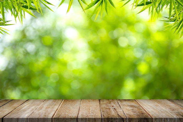 Foto mesa de madera vieja vacía con marco de hojas de bambú sobre fondo verde borroso en el jardín