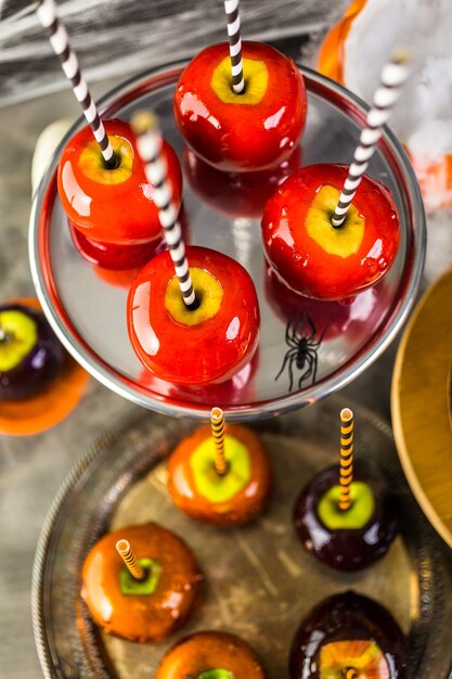 Mesa con manzanas de caramelo de colores y pastel para fiesta de Halloween.