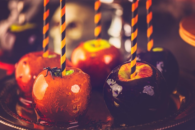 Mesa con manzanas de caramelo de colores y pastel para fiesta de Halloween.