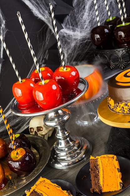 Mesa con manzanas de caramelo de colores y pastel para fiesta de Halloween.