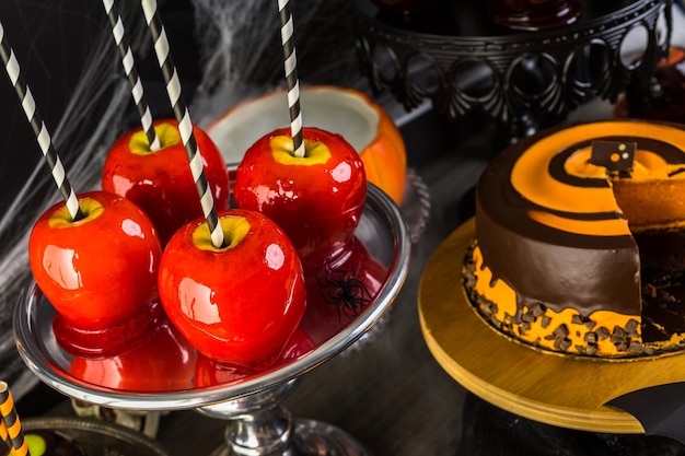 Mesa con manzanas de caramelo de colores y pastel para fiesta de Halloween.