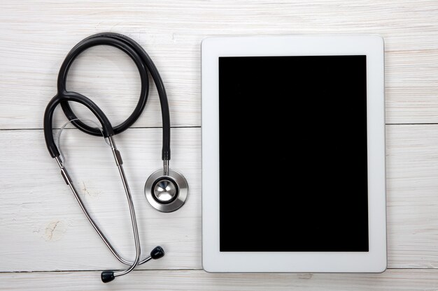 Foto mesa de médicos tablet y estetoscopio azul sobre fondo blanco de madera