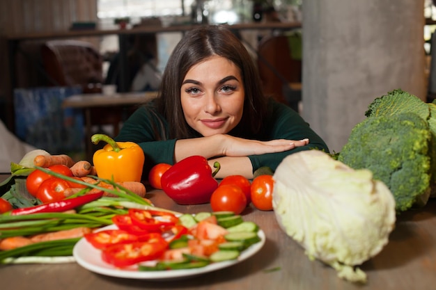 En la mesa con muchas verduras, la mujer está sentada.