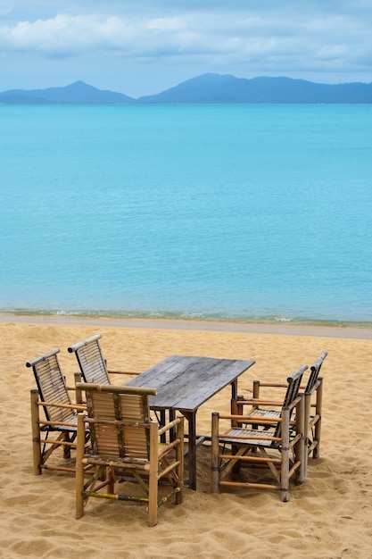 Mesa de muebles de bambú de madera y cinco sillas alrededor de la playa de arena