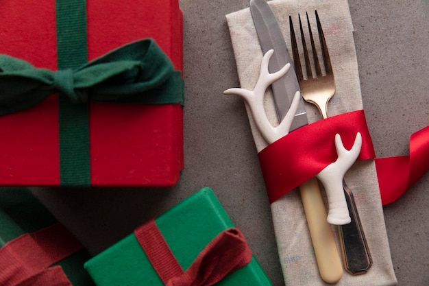 Mesa de Navidad con cubiertos envueltos en una cinta roja y regalos en una caja de regalo