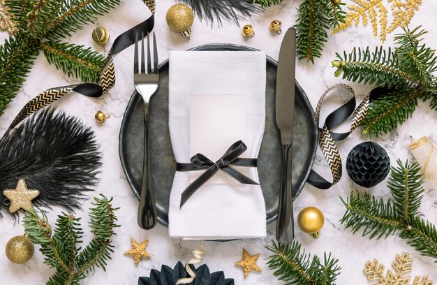 Mesa de Navidad negra y dorada con adornos de tarjetas de lugar y ramas de abeto Mockup