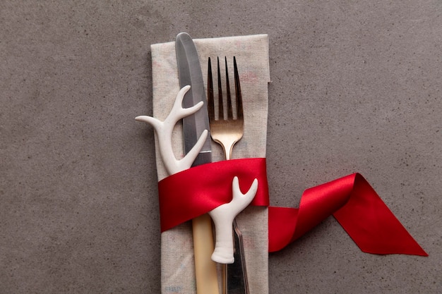 Mesa navideña festiva con cubiertos envueltos en una cinta roja con decoración de cuernos