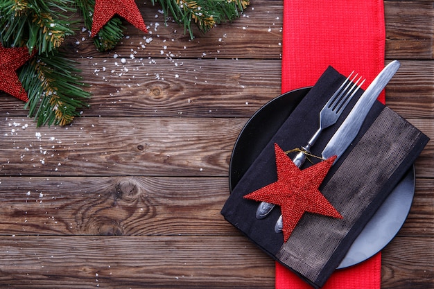 Mesa navideña con plato negro, tenedor y cuchillo, estrella roja decorada