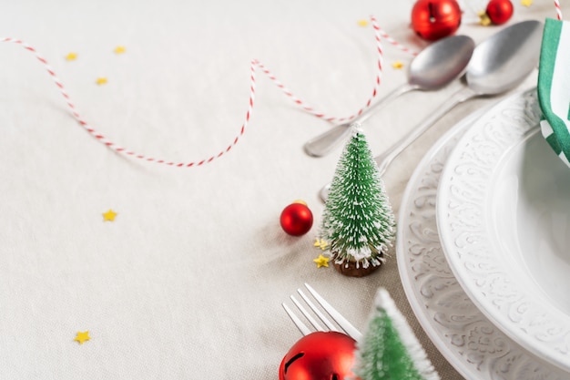 Mesa navideña con platos blancos, cubiertos, servilletas y decoración navideña.