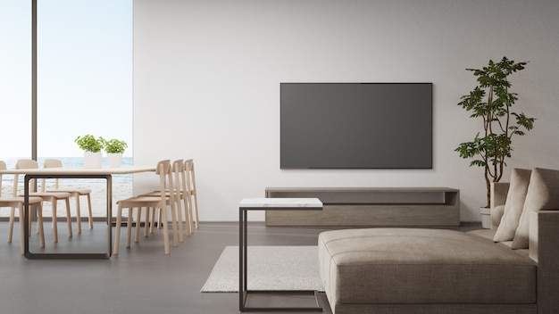 Mesa no piso de concreto da sala de jantar brilhante perto da sala de estar e sofá contra TV na moderna casa de praia ou hotel de luxo.