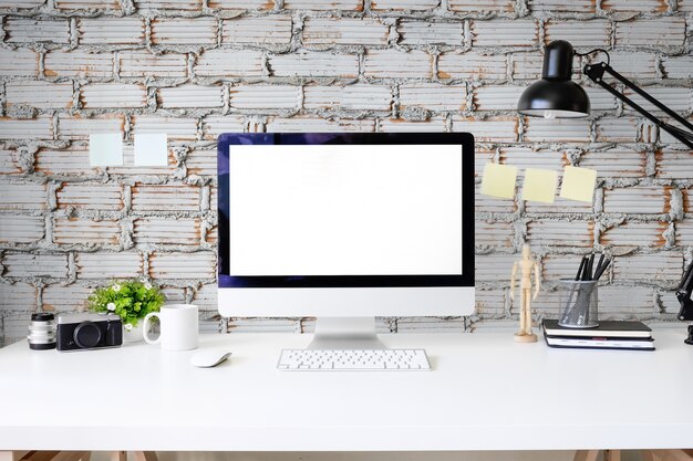 Mesa de la oficina del área de trabajo con pantalla de maqueta de la computadora de la PC en la mesa blanca y pared de ladrillo.