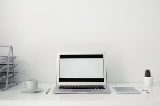 Mesa de oficina en la que se encuentran la computadora portátil, el café, la tableta, la cámara y otros artículos