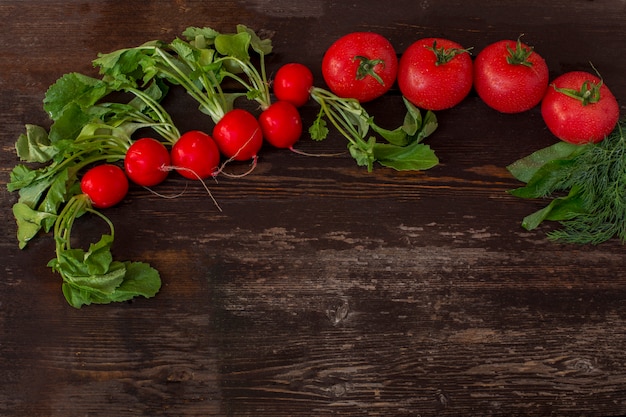 En una mesa oscura, rábano rojo y tomates alineados en una fila.