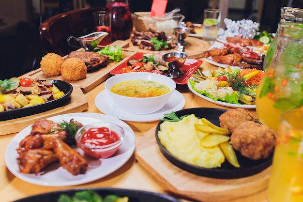 Mesa con parrilla de carne, asado de papas nuevas, verduras, ensaladas, salsas, bocadillos y limonada, vista desde arriba.