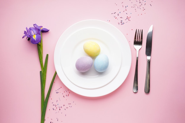 Mesa de Pascua con narcisos y cubiertos sobre una superficie rosa, endecha plana, espacio para texto.