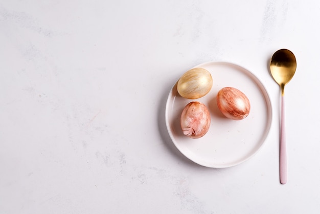 Mesa de Pascua puesta desde arriba. Elegante plato vacío, cubiertos y huevos de oro sobre piedra