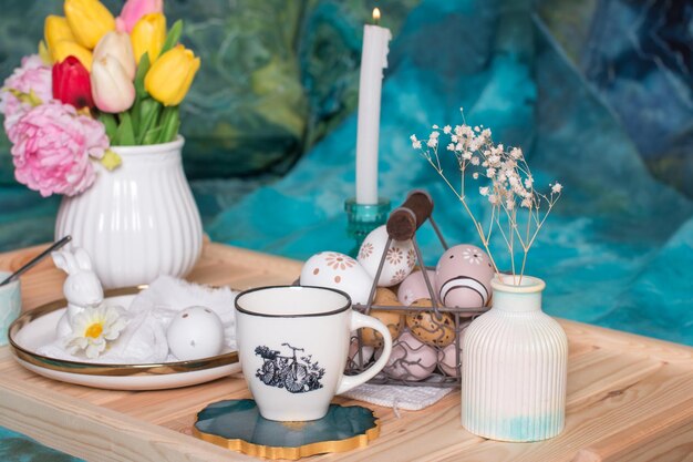 Mesa de Pascua romántica con velas un plato de punto blanco una taza con una bebida Decoración de mesa con conejo y huevos pintados