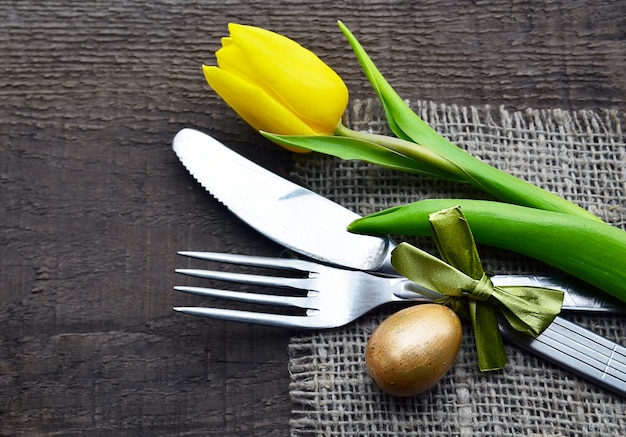 Mesa de Pascua con tulipán amarillo de primavera, huevo y cubiertos en la mesa de madera vieja con espacio de copia. Decoración de Pascua.