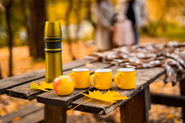 Mesa de picnic con termo y tazas amarillas. Naturaleza de fondo. Camping con termo.