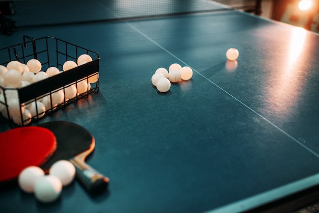 Mesa de ping pong, raquetas y canasta con bolas closeup