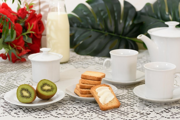 Una mesa con un plato de tostadas de kiwi y una taza de leche.