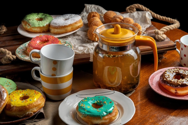 Una mesa con platos en los que yacen donas de todo tipo. Es una tetera con tazas de té.