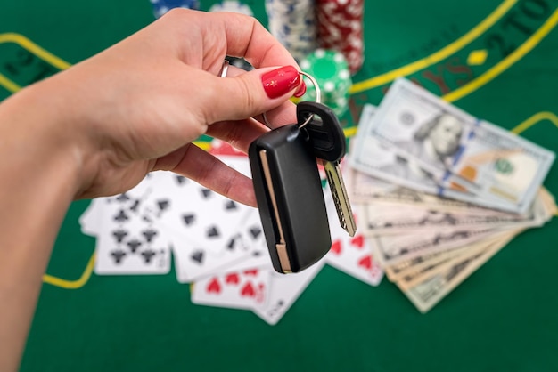 En una mesa de póquer verde hay tarjetas de fichas de dólares y la mano de una mujer sostiene los acantilados del auto